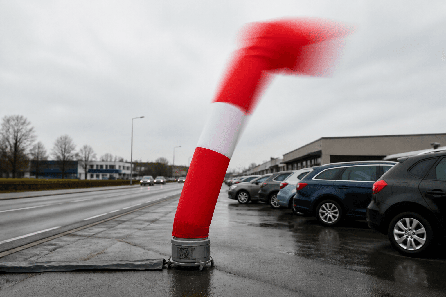 Red and white single-leg air dancer with motion-blurred upper tube beside a vehicle forecourt