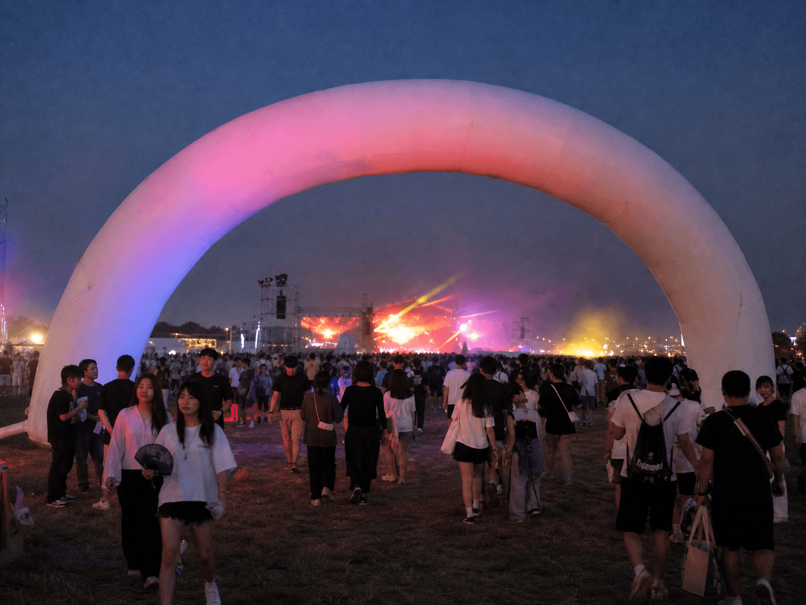 Inflatable entrance arch at a greenfield music festival at dusk with crowd flow and lighting