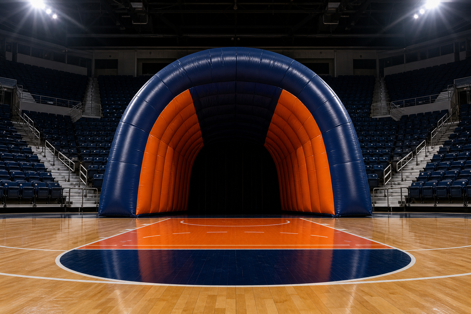 Navy and orange inflatable player entry tunnel set up at the end of an empty basketball court under arena floodlights