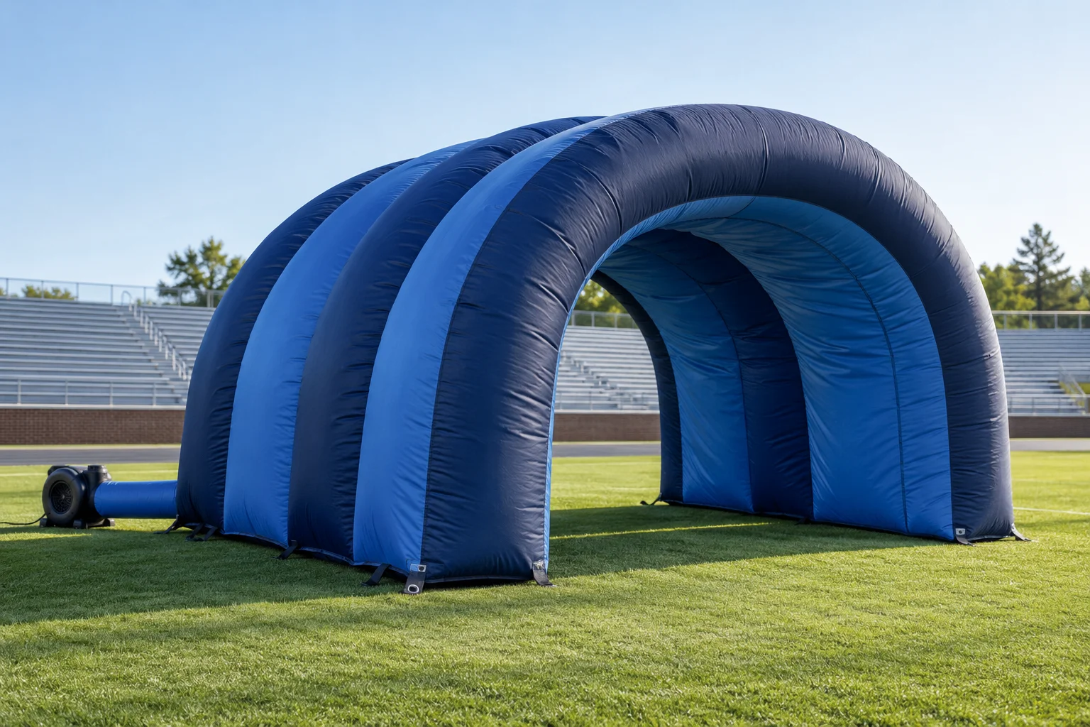 Blue arched inflatable entrance tunnel on a sports field with a separate blower positioned to one side.